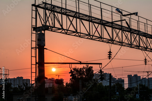 power lines hanging on an iron structure. in the background a city in the sunset light