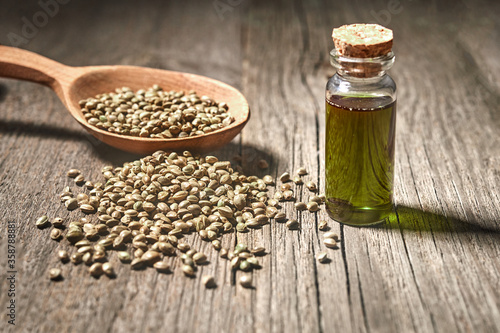 Hemp seeds and hemp oil on wooden table. Hemp seeds in spoon and hemp essential oil in glass bottle.