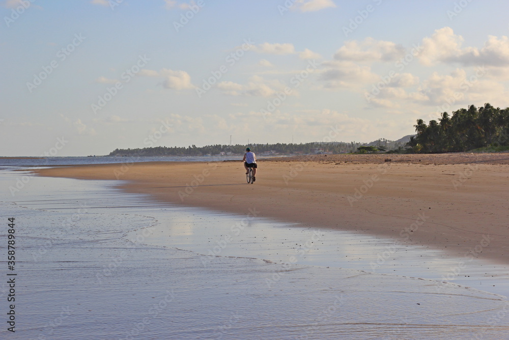 Guarajuba beach, Bahia, Brazil. Open wide beach with a man bicycling. Sand and calm ocean waters. Shot in the early morning before sunrise. 