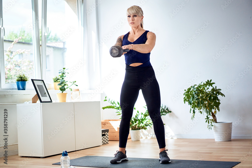 Obraz premium Athletic woman doing swing kettlebell exercise at home