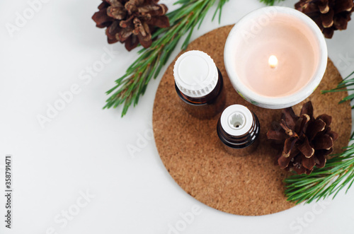 Small glass bottles with essential pine oil and burning candle. Pine branches and cones decoration. Aromatherapy, spa and herbal medicine ingredients. Top view, copy space.