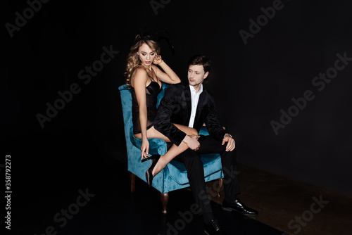 Handsome man touching sensual woman in bunny ears in armchair isolated on black