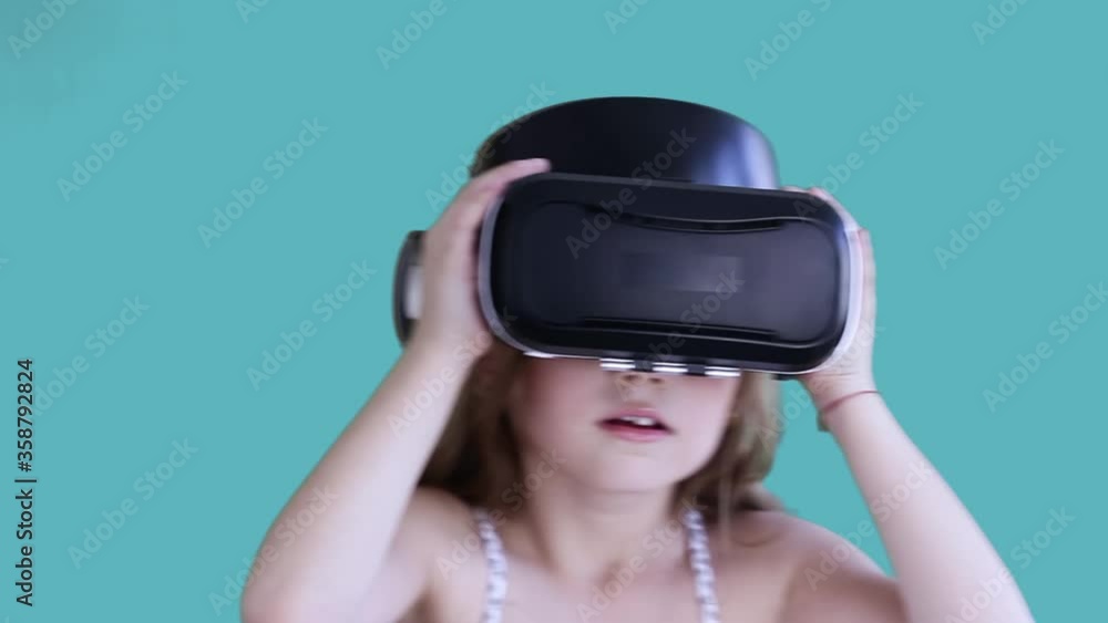 Caucasian girl watching simulation in virtual reality googles, moving, impressed by VR googles. Concept of modern technology. Isolated on blue background Caucasian girl watching simulation in virtual reality googles, moving, impressed by VR googles. Concept of modern technology. Isolated on blue background