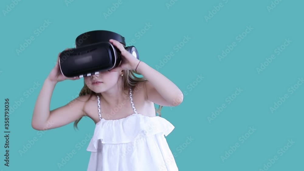 An isolated cute beautiful kid in white dress wearing VR glasses, moving energetically, putting off this helmet, looking scared at camera. Concept of lifestyle. An isolated cute beautiful kid in white dress wearing VR glasses, moving energetically, putting off this helmet, looking scared at camera. Concept of lifestyle.