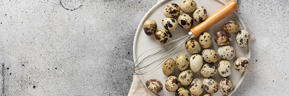 Fototapeta premium Quail eggs in a white plate on the kitchen table. Quail eggs m Corolla on a culinary background. Concept of preparation for baking. Top view with space for text. Banner