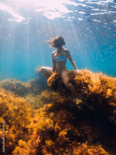 Woman freediver posing on stone with seaweed in underwater. Freediving in ocean