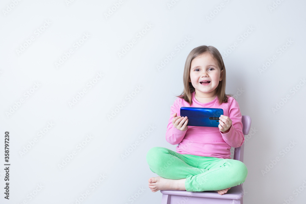 Beautiful caucasian girl watching a cartoon on a smartphone. Very surprised. Gray background. Beautiful caucasian girl watching a cartoon on a smartphone. Very surprised. Gray background.