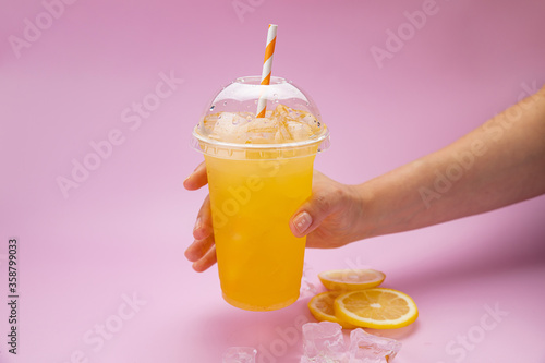 Summer Drink Fresh Lemonade with orange in the plastic cup on a pink background