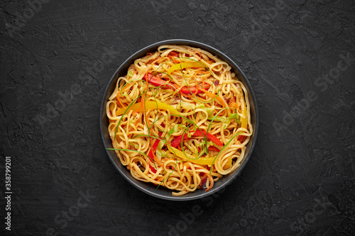 Chilli Garlic Hakka Noodles in black bowl on dark slate tabpe top. Indo-Chinese vegetarian cuisine dish. Indian veg noodles with vegetables. Classic Asian meal. Copy space. Top view