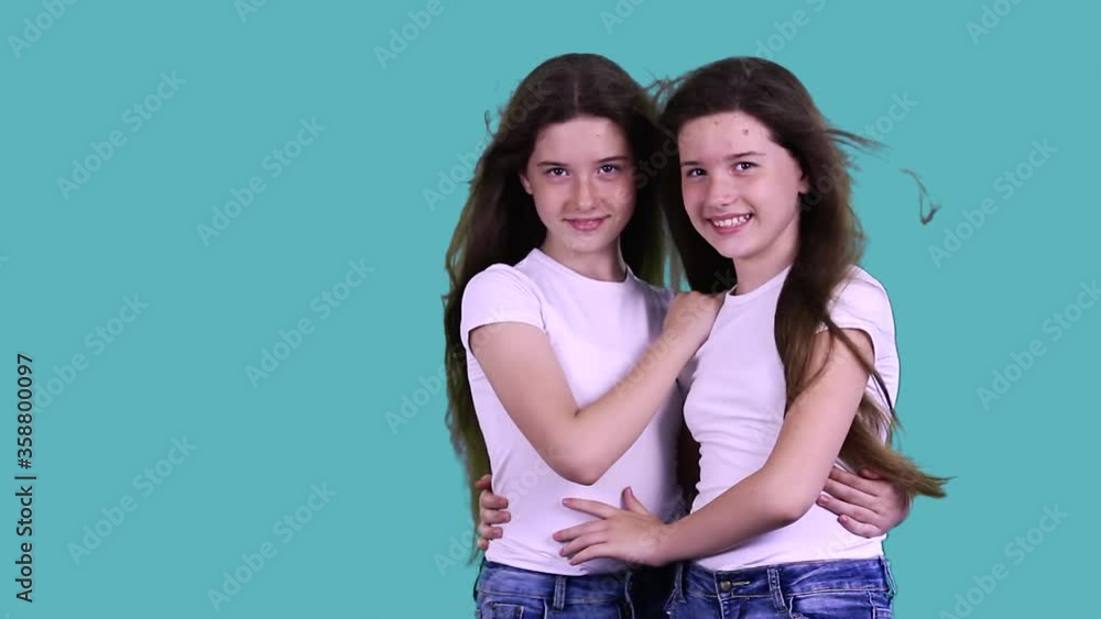 Attractive adorable cheerful pretty little sisters having their long hair wafting stand together holding each other in hugs, smile, look at the camera. Family and childhood concept. Attractive adorable cheerful pretty little sisters having their long hair wafting stand together holding each other in hugs, smile, look at the camera. Family and childhood concept.
