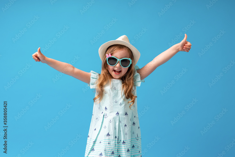 cute little girl in a dress, hat and sunglasses poses on a blue ...