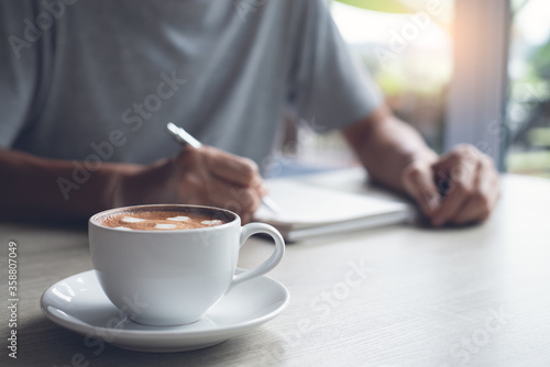 Casual man writing notes on paper notebook in coffee shop