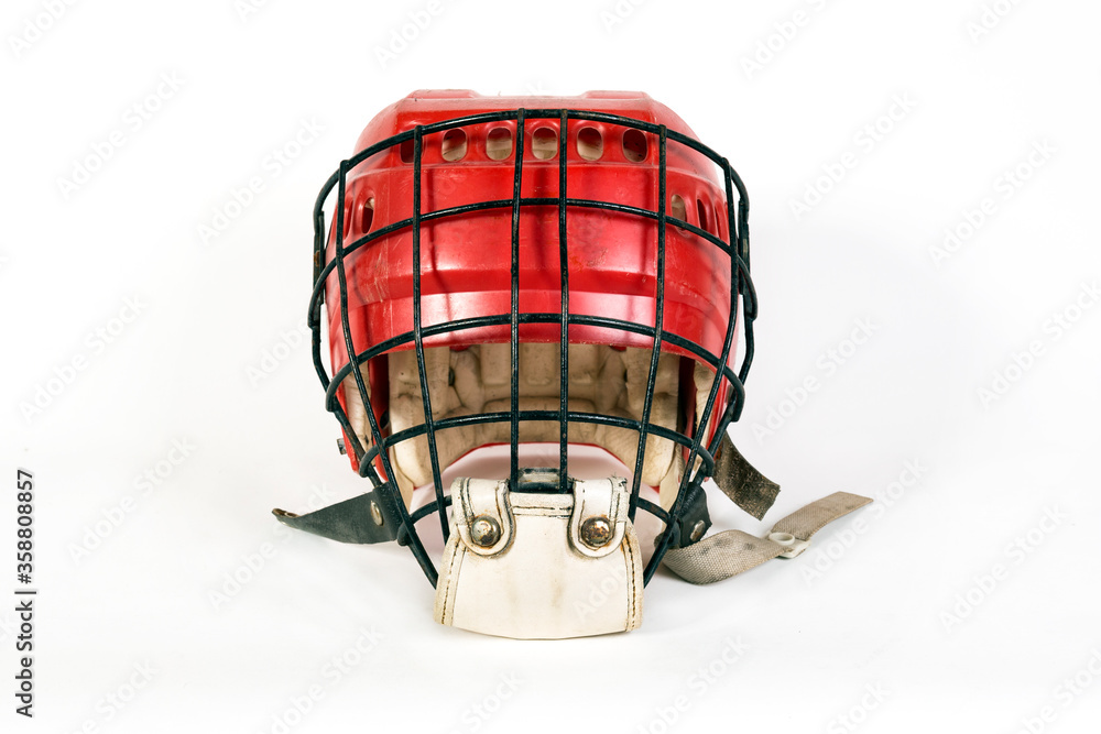 An old hockey helmet of red color with a protective iron mask on a white background An old hockey helmet of red color with a protective iron mask on a white background