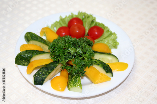 Sliced vegetables on a plate: tomato, cucumber and red pepper and green salad leaves