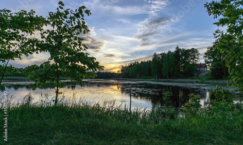 Fototapeta Naklejka Na Ścianę i Meble -  image with a beautiful colorful sunset over the lake, in the foreground the contours of trees and grass, Lielais Ansis, Rubene, Latvia