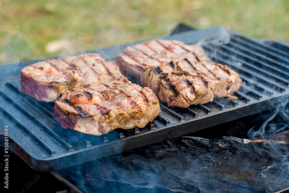 Beef steaks grilling on a cast iron plate on a camp fire. Campfire cooking. Outdoor BBQ.