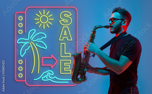 Young jazz musician playing the saxophone on gradient studio background in neon light neon sign SALE. Concept of music, hobby, festival. Joyful inspired artist, flyer. Summertime, sale, vacation.