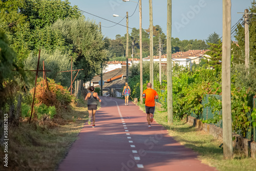 View of eco pedestrian / cycle lane, people running and walking with dog, trees village as background