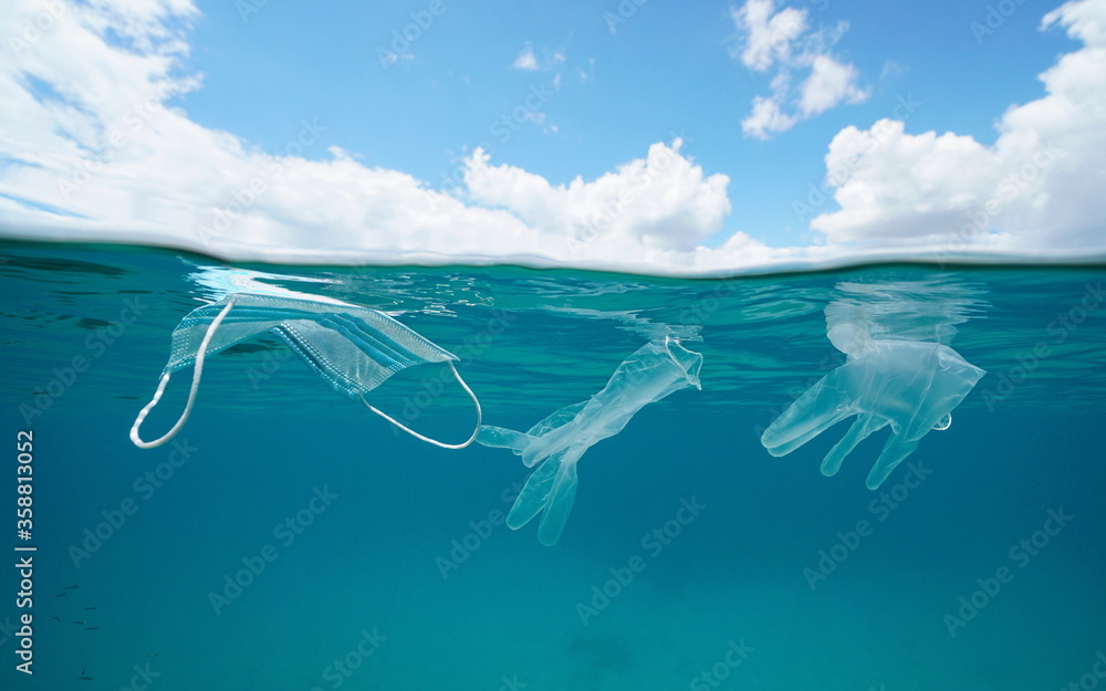 Fototapeta premium Plastic waste pollution underwater since coronavirus COVID-19 pandemic, face mask with gloves in the ocean and blue sky with cloud, split view over and under water surface