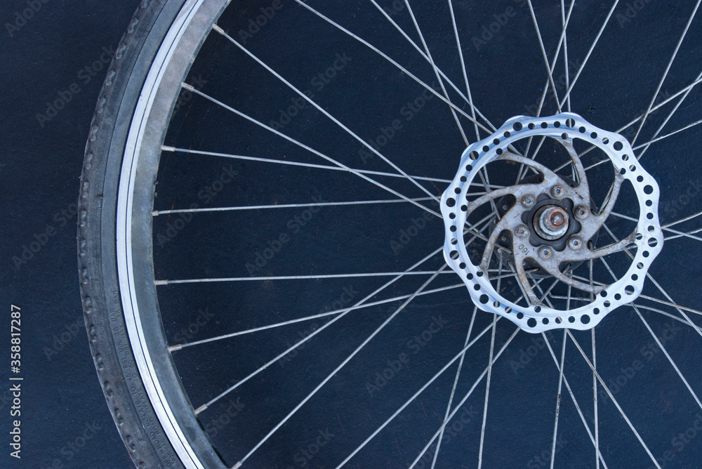 Single silver new bicycle wheel on a monochromatic (dark blue) background.