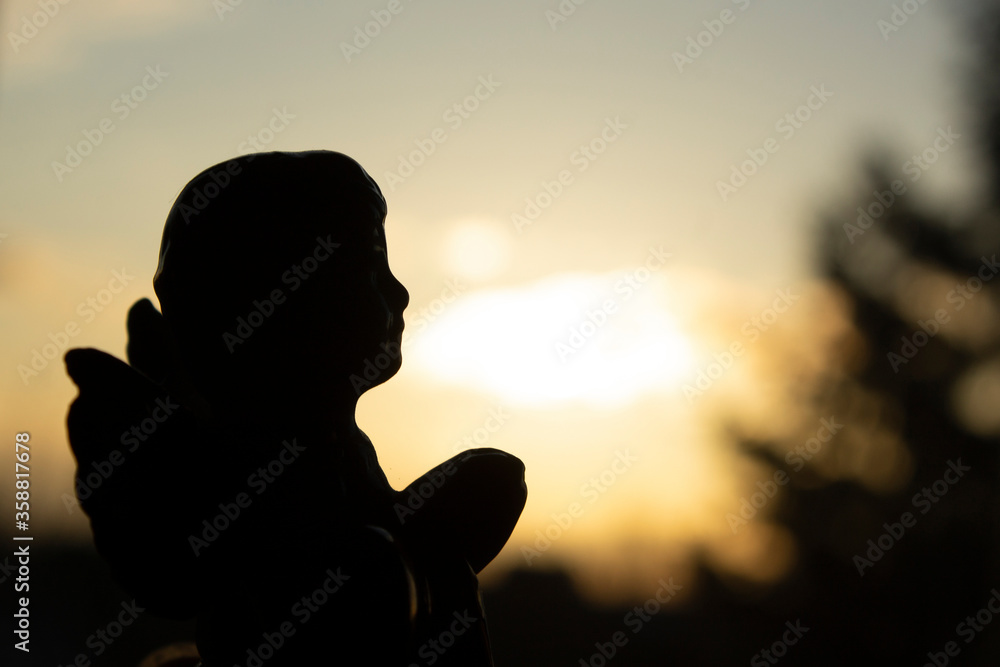Silhouette of praying angel figurine in the sunset sky background
