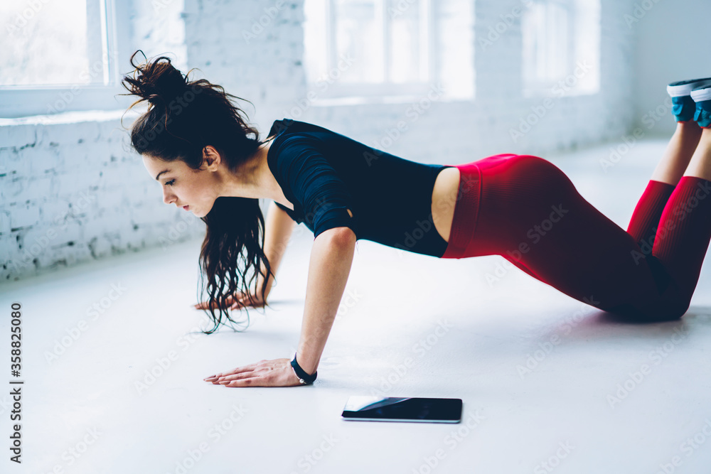Determined woman doing push ups exercises for training chest and arms  muscles in white interior gym,slim strong girl planking from knees having  hard workout for keeping athletic body shape Stock Photo