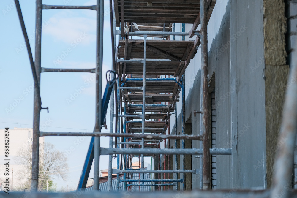 Fototapeta premium Empty scaffolding near the building with spread out work items - ropes, buckets, uniforms and a ladder