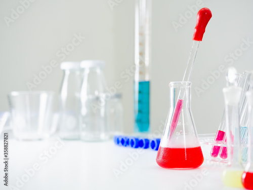 Triangular shape flask With red water and a chemical straw inside There is steam on the side of the bottle. There are much experimental equipment behind and besides In the white lab with copy space