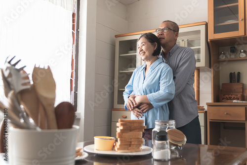 Elderly couple Standing together, hugging from behind, looking forward happily