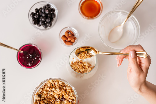 Hand of young woman with teaspoon putting muesli into glass with fresh sourcream