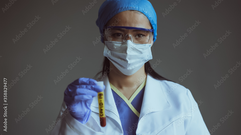 Lab assistant holds test tube with blood on blured foreground. Female worker of medical lab isolated on gray backgrund. Close up shot. Toned image. Lab assistant holds test tube with blood on blured foreground. Female worker of medical lab isolated on gray backgrund. Close up shot. Toned image.