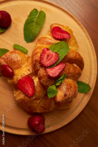 Croissants on a wooden board with strawberries. Perfect breakfast. Crispy croissants with berries and mint.