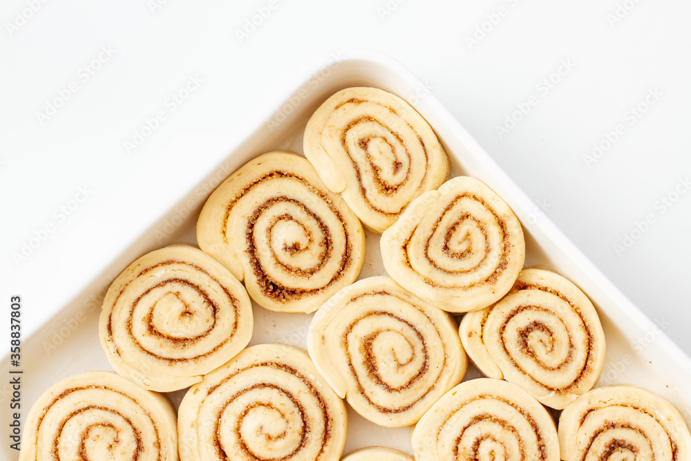 Close-up of Tasty raw cinnamon rolls in baking dish on white table