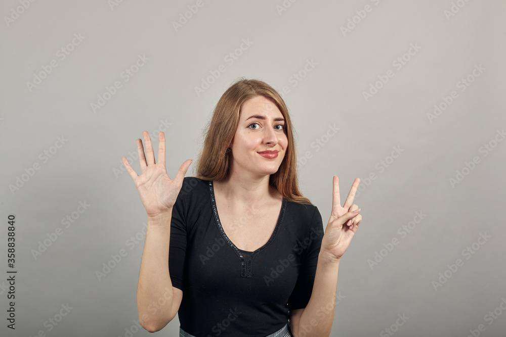 Showing 7 fingers hand gesture, show the number three with hands, pointing up arm while smiling confident, happy. young attractive woman, dressed black t-shirt, grey background Showing 7 fingers hand gesture, show the number three with hands, pointing up arm while smiling confident, happy. young attractive woman, dressed black t-shirt, grey background