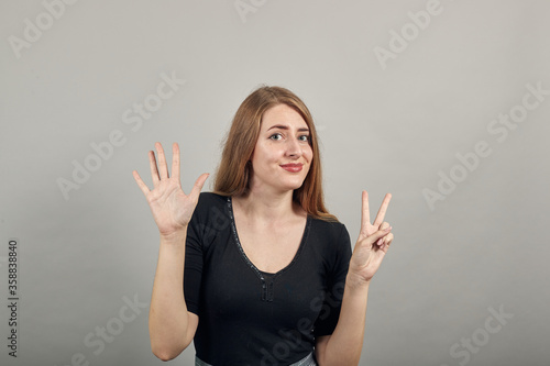 Showing 7 fingers hand gesture, show the number three with hands, pointing up arm while smiling confident, happy. young attractive woman, dressed black t-shirt, grey background