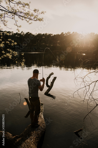 Rear view of man fishing in lake while standing on tree trunk