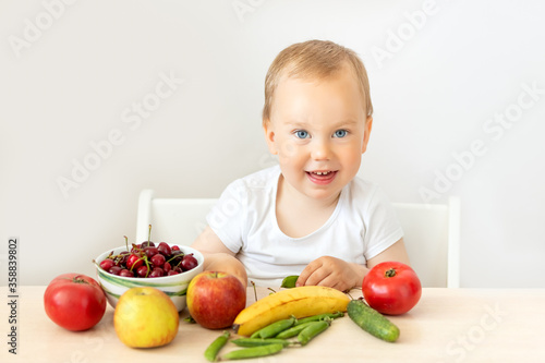 baby boy 2 years old sitting at a table on a white isolated background and eating fruits vegetables, baby food concept, place for text