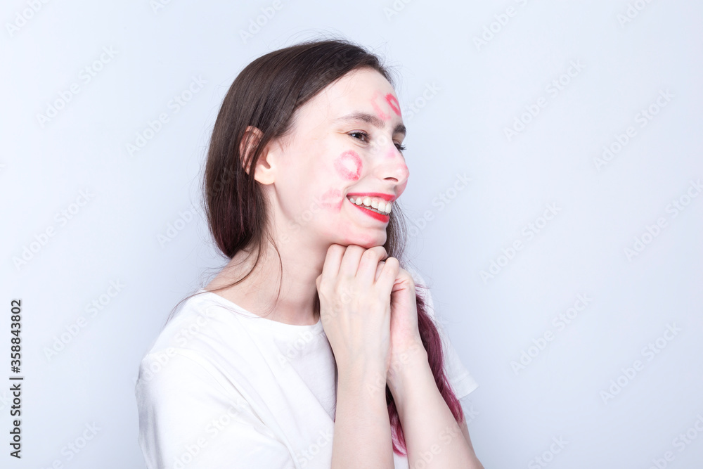 Happy young girl with kisses imprints on her face with red lipstick. World Kissing Day Concept Happy young girl with kisses imprints on her face with red lipstick. World Kissing Day Concept
