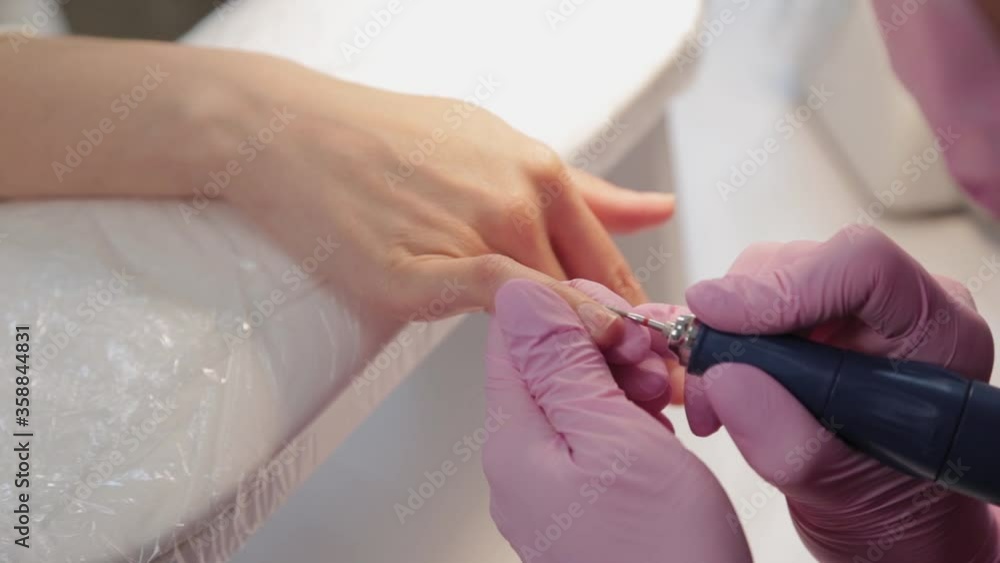 Manicurist cuts nails with a machine to a client in a manicure salon. Manicurist cuts nails with a machine to a client in a manicure salon.