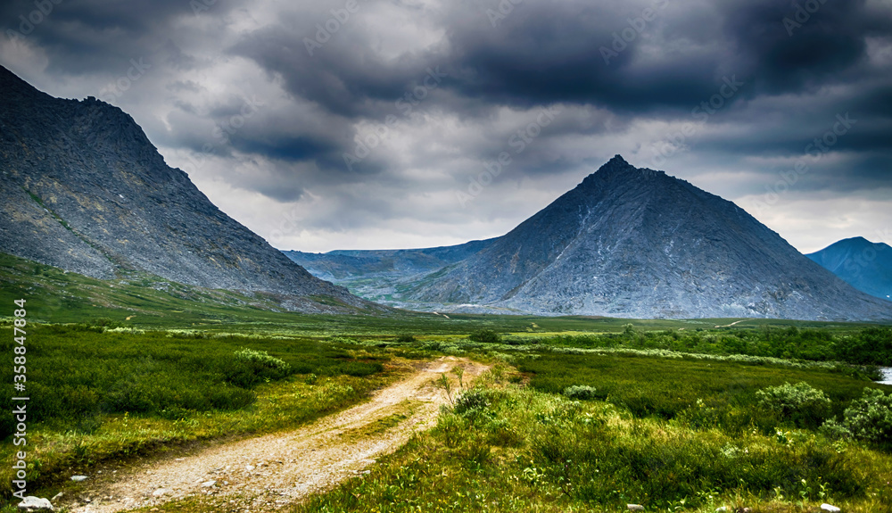 gravel road to mountain ridge with cloudy gray summer sky, Panoramic landscape of Ural mountains, Russia
