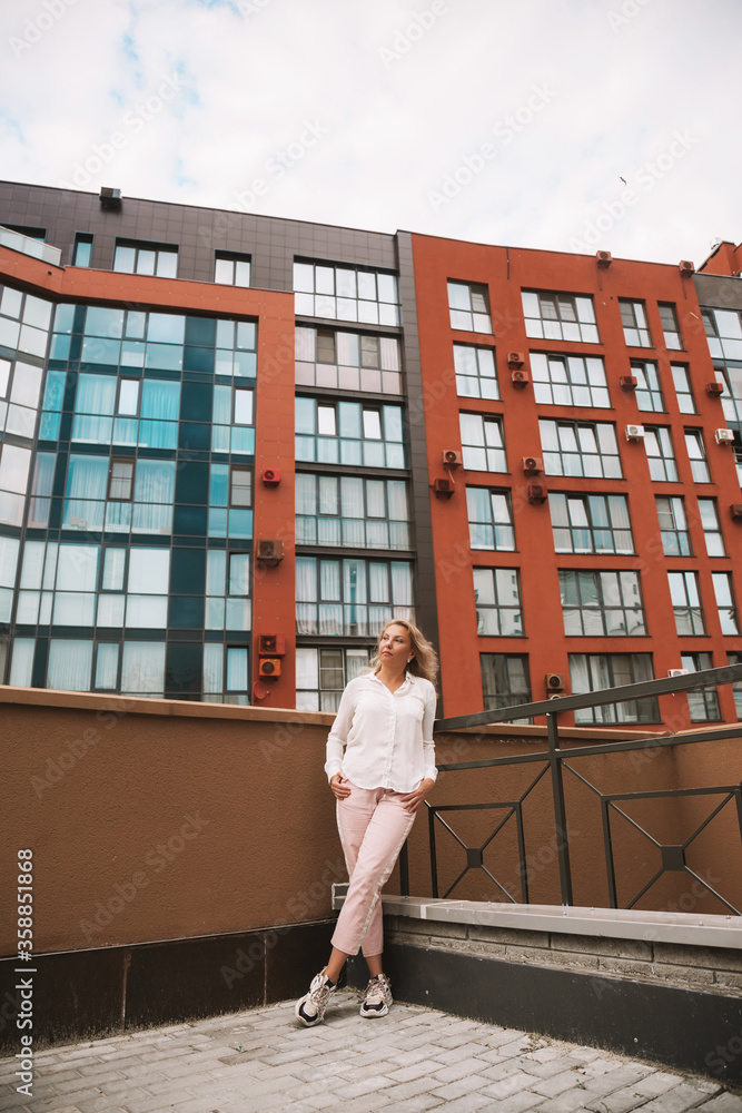 Full length portrait of stylish pretty cheerful blonde woman posing on the street near business center buildings