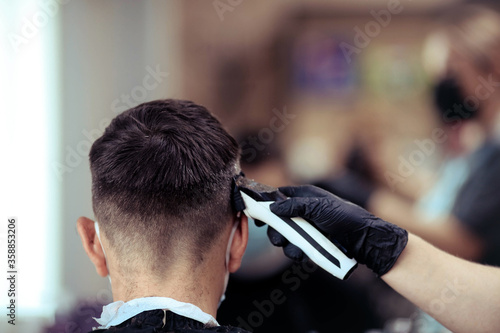 A hairdresser with security measures for Covid-19, holds a razor and a haircut for a man, talks at a distance, cuts his hair with rubber gloves