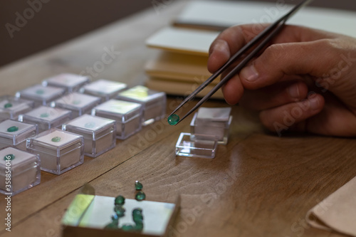 Hand holding a emerald gemstone with jewelry forceps. Gemologist workspace.
