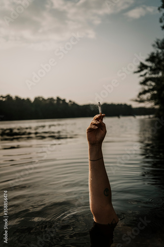 Woman's hand holding cigarette while swimming in lake