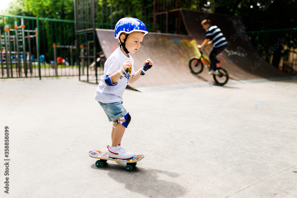 Fototapeta premium Boy with a skate in a skate park. The boy learns to skate, in full protection.