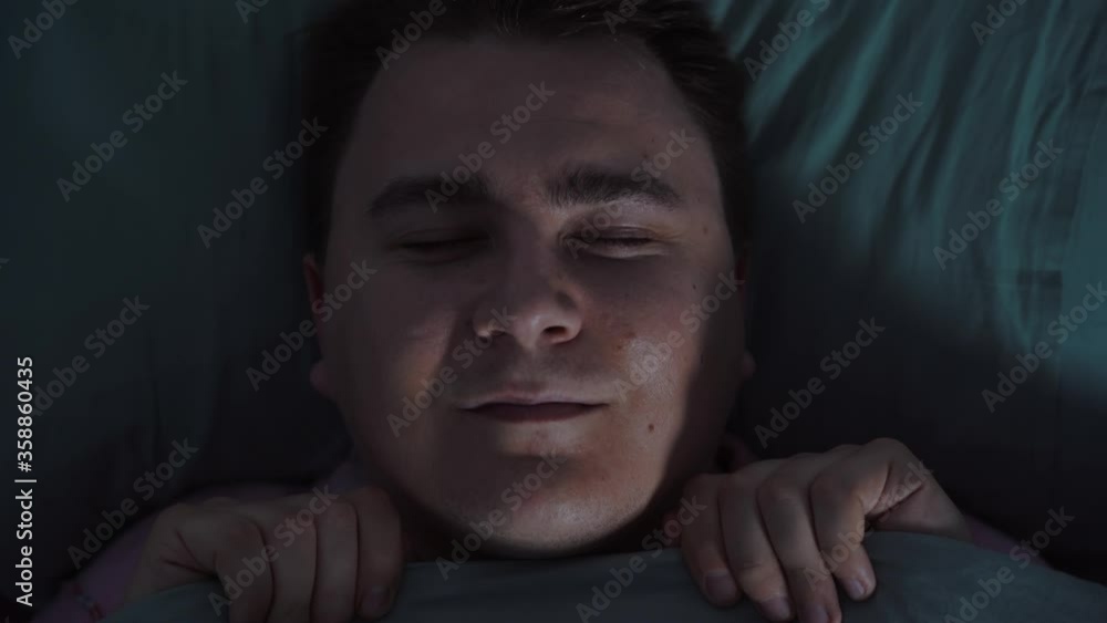 Man sleeps sweetly in bed, hiding to chin with warm blanket, he suddenly hears strange noise, wakes up, sharply opens his eyes and looks up in dismay, trying to understand what happened. Man sleeps sweetly in bed, hiding to chin with warm blanket, he suddenly hears strange noise, wakes up, sharply opens his eyes and looks up in dismay, trying to understand what happened.