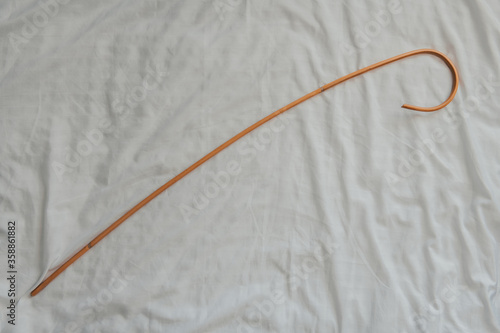 Rattan cane with crooked handle on white background top view. Dragon rattan cane for spanking. Traditional corporal punishment. Home child abuse.