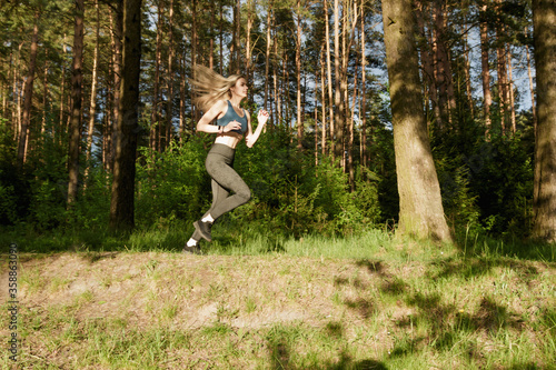 Young slim athletic woman getting ready for a marathon while running through the forest