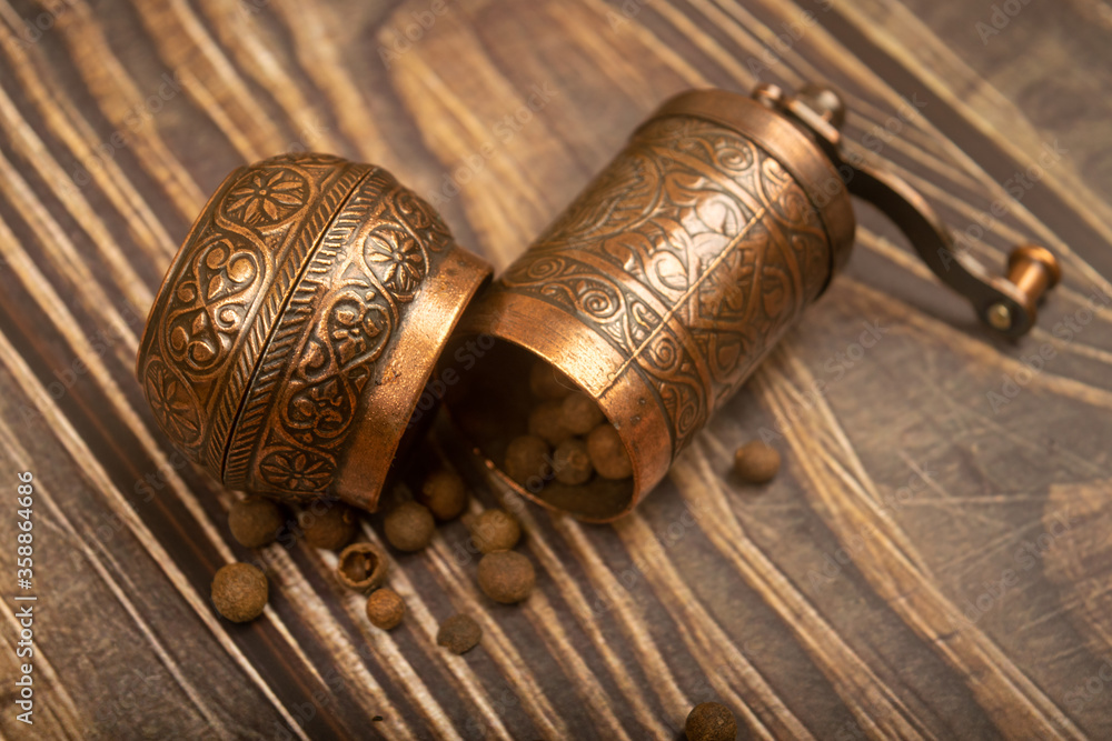 An open manual spice mill and a scattering of ground allspice on a wooden table. Close up. An open manual spice mill and a scattering of ground allspice on a wooden table. Close up.