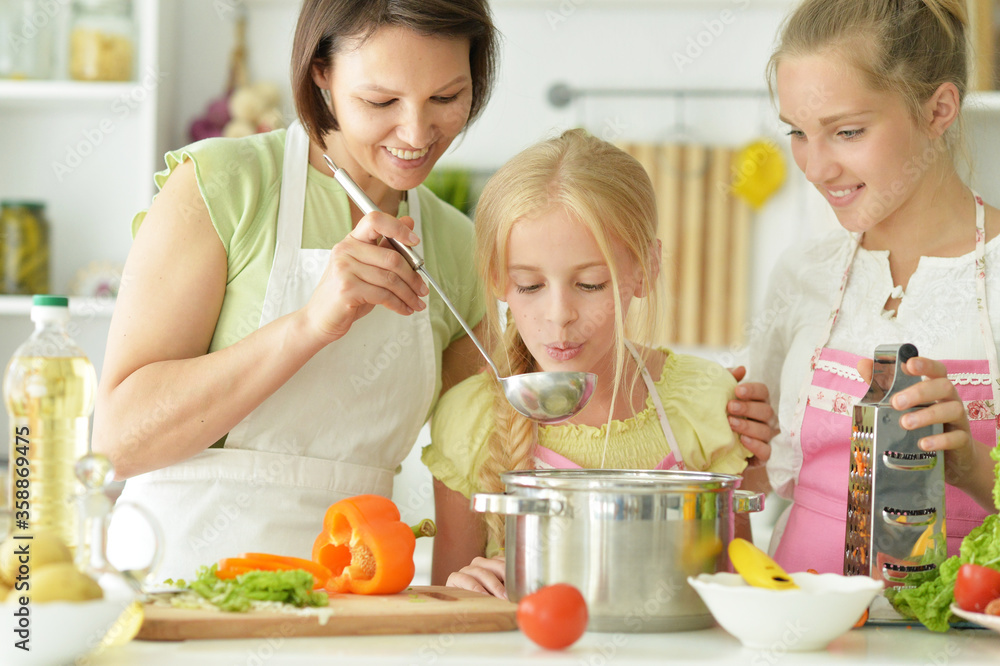 Cute girls with mother preparing delicious fresh salad in kitchen Cute girls with mother preparing delicious fresh salad in kitchen